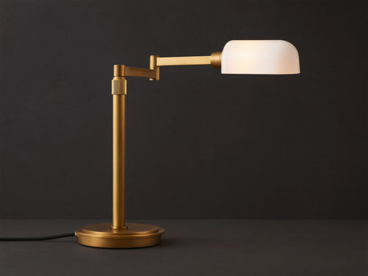 Zayd Swing Arm Table Lamp with brass finish and illuminated white opal glass shade, on a wooden table.