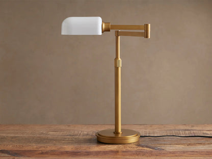 Zayd Swing Arm Table Lamp with brass finish and illuminated white opal glass shade, positioned on a rustic wooden table.