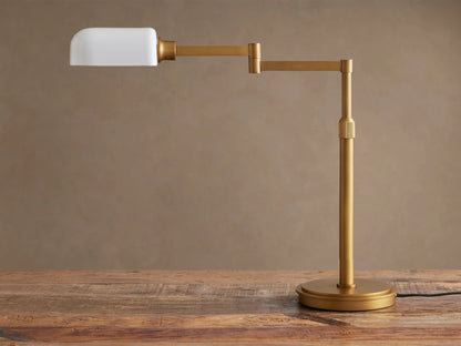 Brass Zayd Swing Arm Table Lamp with white opal glass shade, adjustable arm extended, on a wooden table.