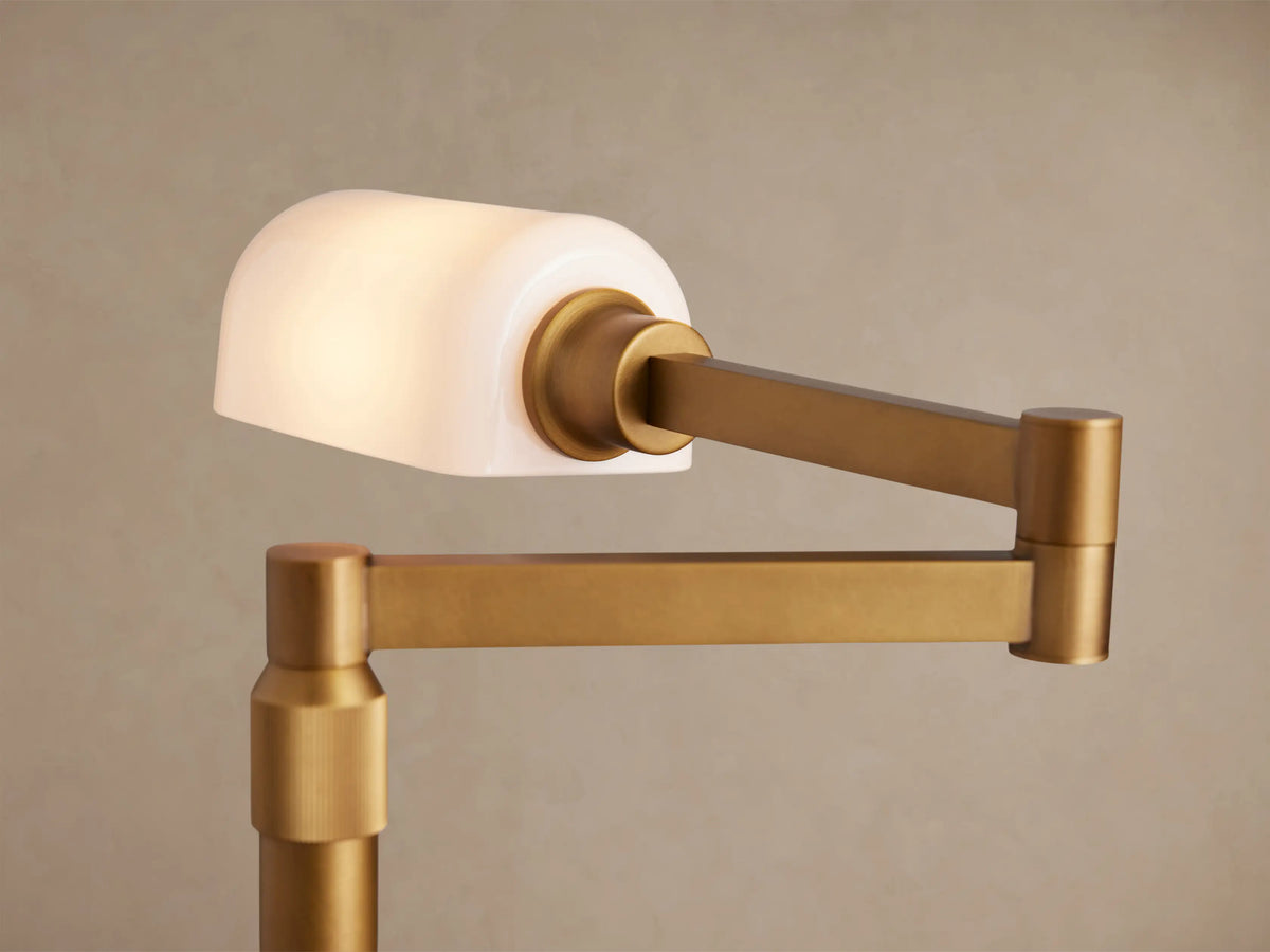 Zayd Swing Arm Table Lamp in golden brass with an opal glass shade, adjustable arm extended left, on a rustic wooden table.