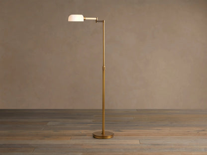 Zayd Swing Arm Floor Lamp, brass with an extended arm, illuminated opal glass shade, on a wooden floor.