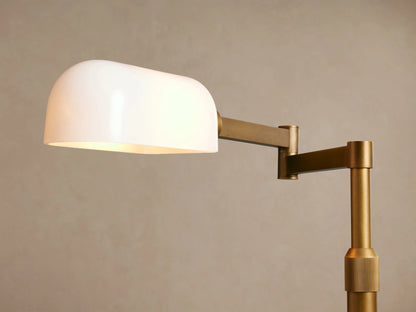 Tall brass Zayd Swing Arm Floor Lamp with a round base, L-shaped arm, and rectangular white opal glass shade, on a wooden floor.