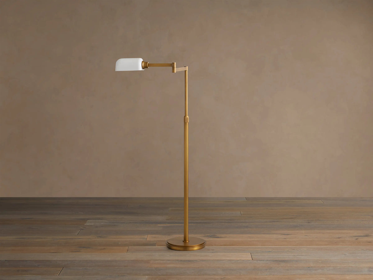Zayd Swing Arm Floor Lamp with golden brass finish, white opal glass shade, standing on a wooden floor.
