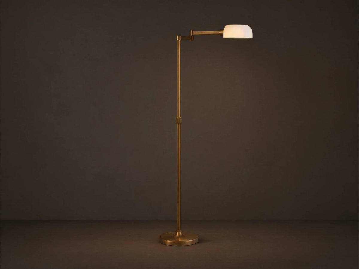 Zayd Swing Arm Floor Lamp, brass with an extended arm, illuminated opal glass shade, on a wooden floor.