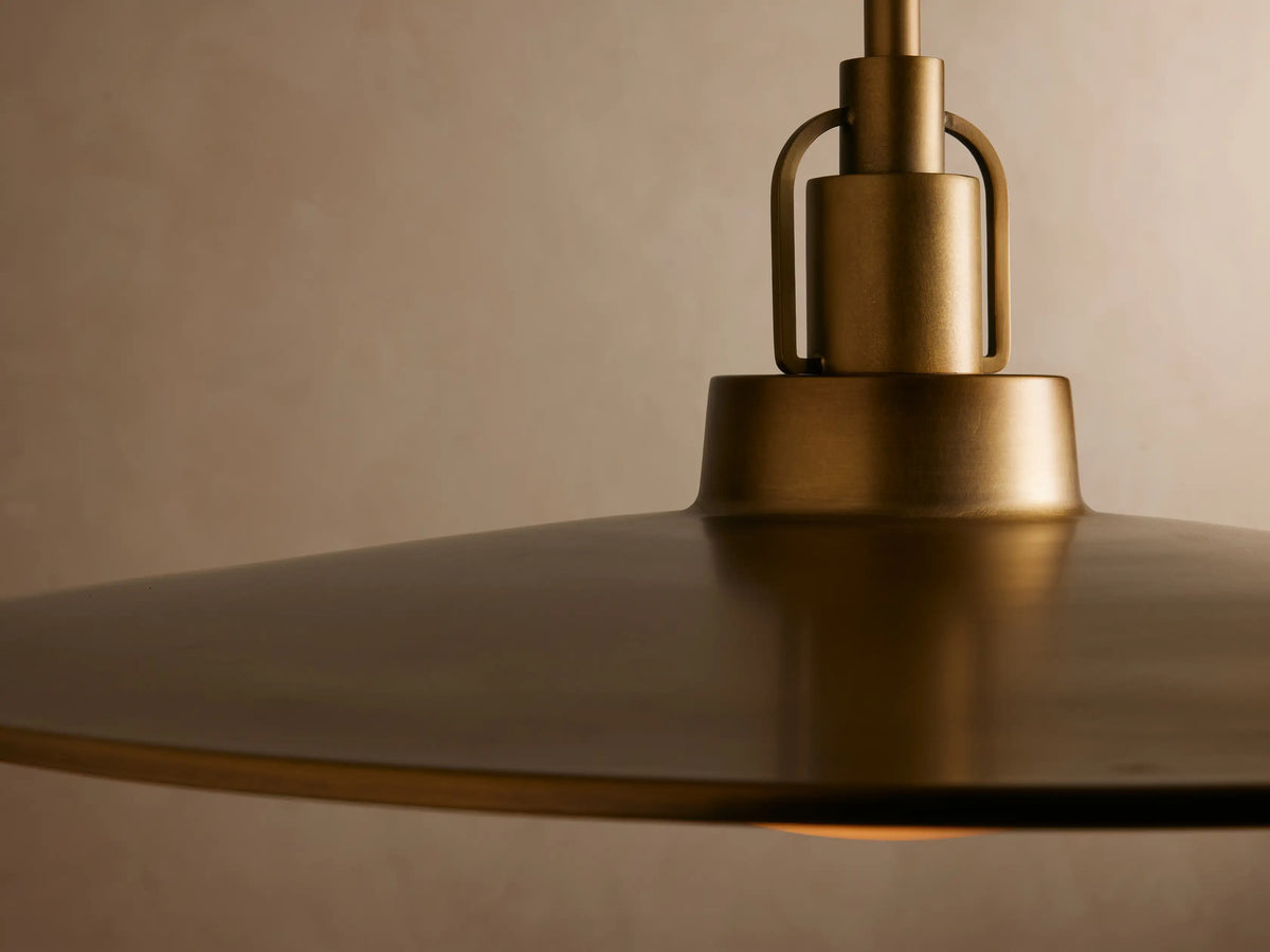 A close-up of a modern pendant light with a warm, glowing amber glass shade and a brass finish, suspended from a ceiling.