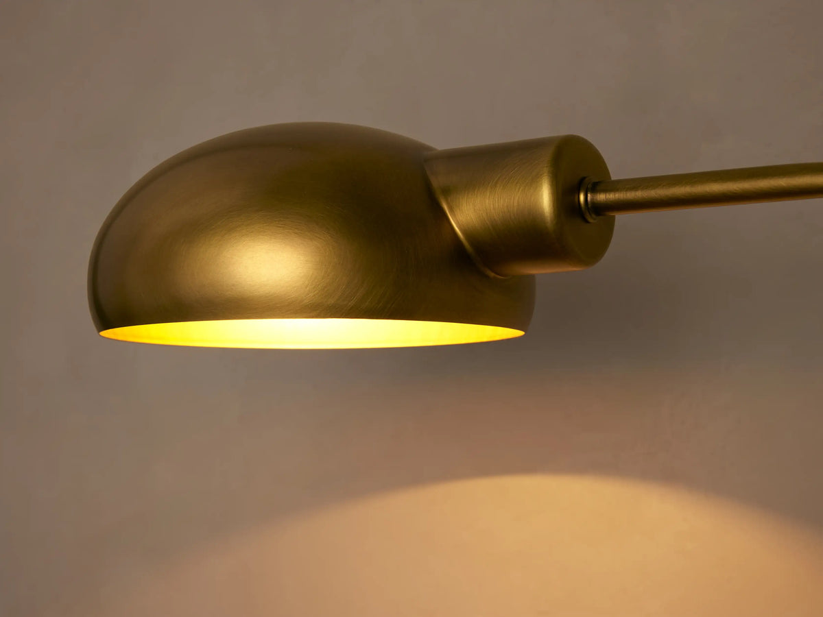 Bergamo Task Table Lamp, brass finish, domed shade, curved arm, and round base on a wooden table next to books.