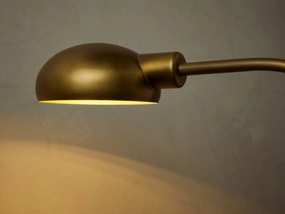 Close-up of the Bergamo Task Table Lamp's dome-shaped brass shade, emitting a warm yellow glow downwards onto a muted wall.