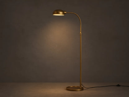 Sleek brass Bergamo Task Floor Lamp with illuminated, pivoting shade, standing on wood floor against a textured wall.
