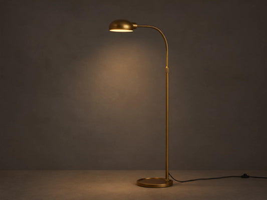 Sleek brass Bergamo Task Floor Lamp with illuminated, pivoting shade, standing on wood floor against a textured wall.