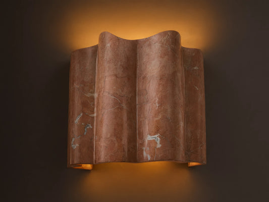 Faine Sconce, a wavy reddish-pink marble wall light with natural white veining, casts a warm glow upwards and downwards.