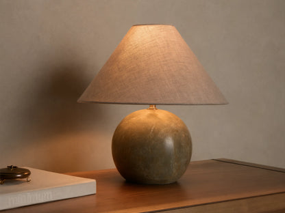 Front view of a table lamp with a round, mottled dark green stone base and an illuminated light brown conical fabric shade.