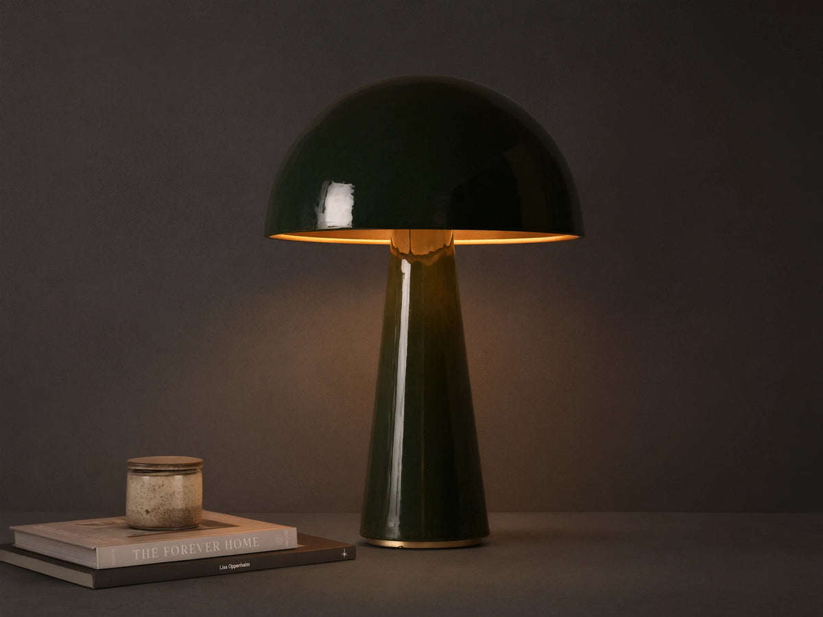 Dark green mushroom-shaped table lamp with brass interior shade, on a wooden surface, emitting warm light.