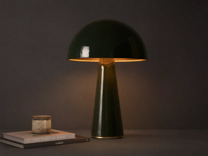 Dark green mushroom-shaped table lamp with brass interior shade, on a wooden surface, emitting warm light.