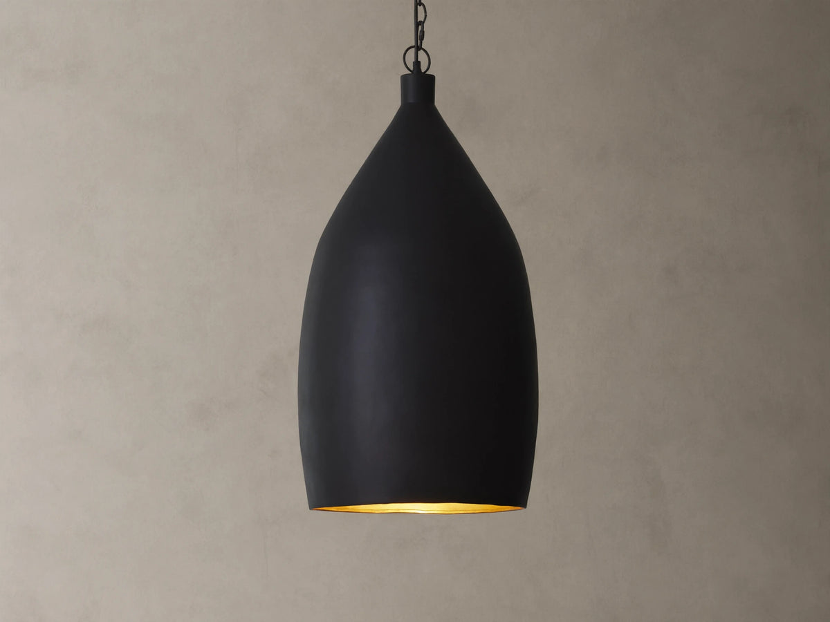 A matte black pendant light with a smooth, teardrop shape hanging from a chain against a beige textured wall.