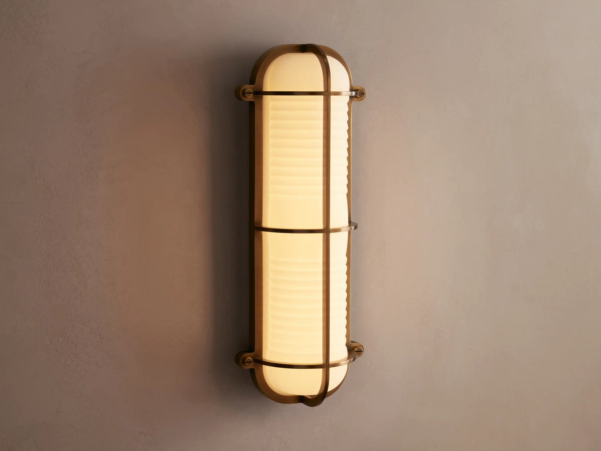 Solomon Outdoor Sconce, vertical, brass-framed, with glowing ribbed milk glass diffuser mounted on a neutral-colored wall.