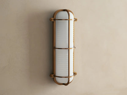 Solomon Outdoor Sconce, vertical, brass-framed, with glowing ribbed milk glass diffuser mounted on a neutral-colored wall.