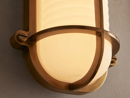 Solomon Outdoor Sconce with a brass frame and ribbed white milk glass diffuser, mounted vertically on a light beige wall.