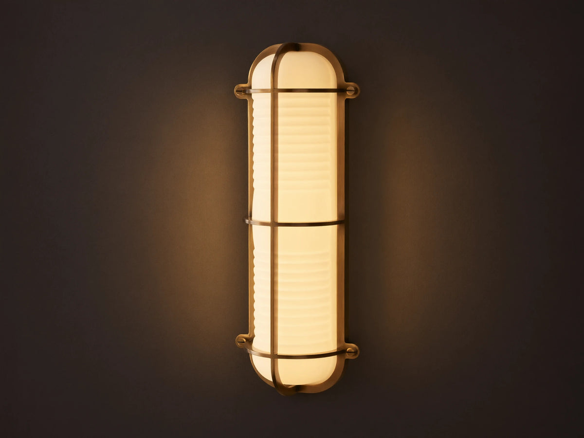Solomon Outdoor Sconce, vertical, brass-framed, with glowing ribbed milk glass diffuser mounted on a neutral-colored wall.