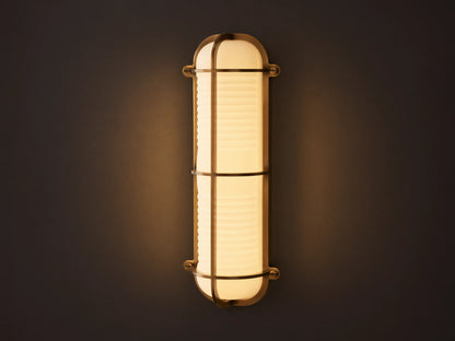 Solomon Outdoor Sconce, vertical, brass-framed, with glowing ribbed milk glass diffuser mounted on a neutral-colored wall.