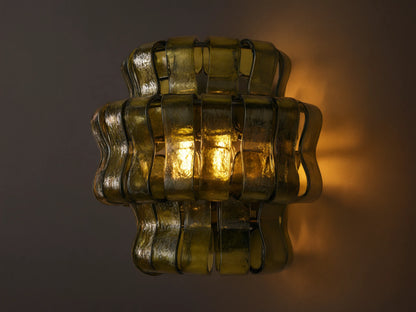 Ghiaccio Sconce: Dark green wavy textured glass wall sconce, glowing warmly, mounted on a light-colored wall.