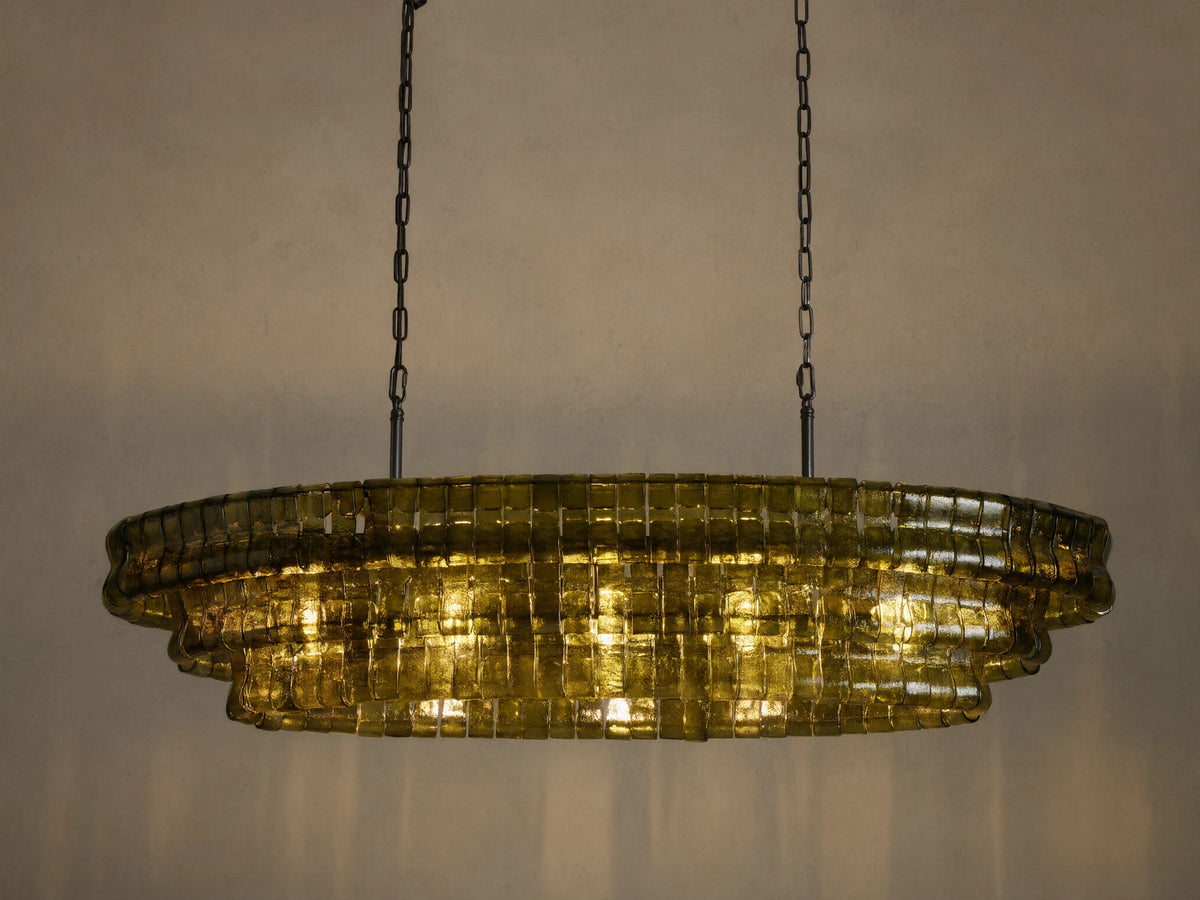Ghiaccio Oval Chandelier, olive green curved glass squares in a tiered oval design, illuminated brightly, hanging from dark chains.