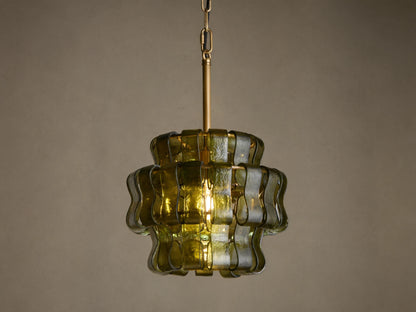 Ghiaccio Pendant, a tiered dark green wavy curved glass pendant light with brass chain, glowing warmly against a neutral wall.