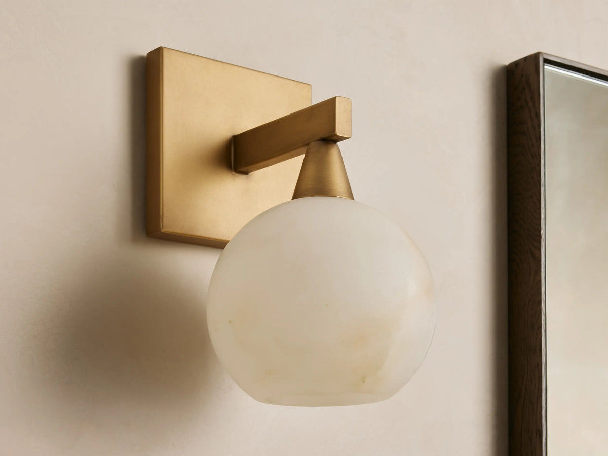 Front view of a brass wall light with a square backplate, horizontal arm, and glowing, translucent white veined globe shade.