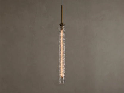 Vertical view of a lit pendant light with a clear textured glass cylinder, a warm filament bulb, and a brass-colored top fixture.