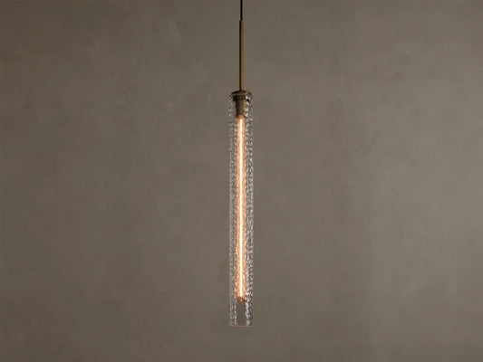 Vertical view of a lit pendant light with a clear textured glass cylinder, a warm filament bulb, and a brass-colored top fixture.