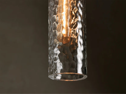 Close-up of a clear hammered glass pendant light with antique brass cap, showing a warm glowing bulb inside.