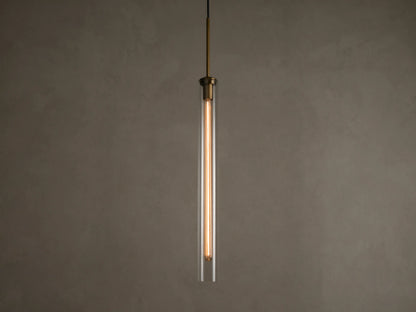 Front view of a modern brass and clear glass pendant light fixture with a long, illuminated filament bulb inside.