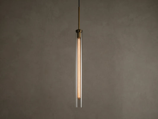 Front view of a modern brass and clear glass pendant light fixture with a long, illuminated filament bulb inside.