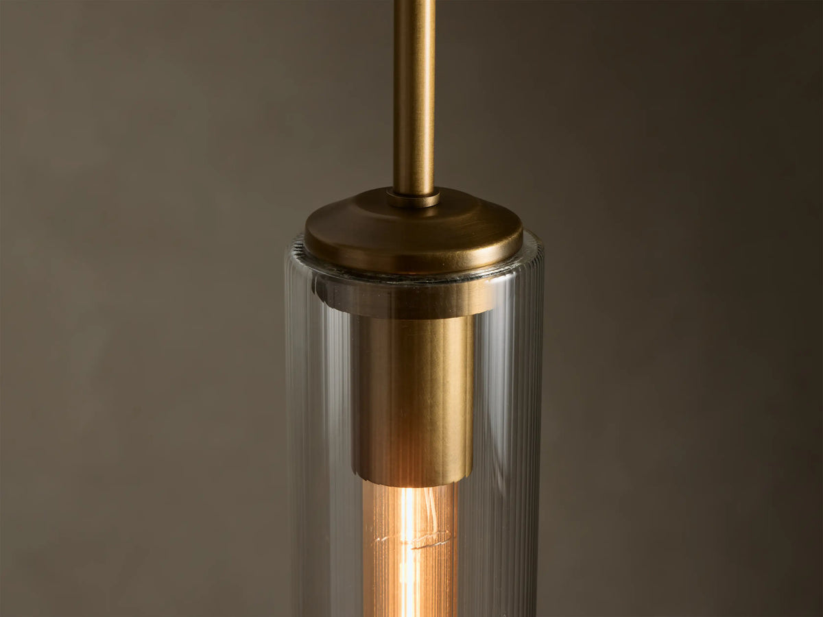 Close-up of a brass pendant light with a fluted clear glass shade and a glowing exposed filament bulb.