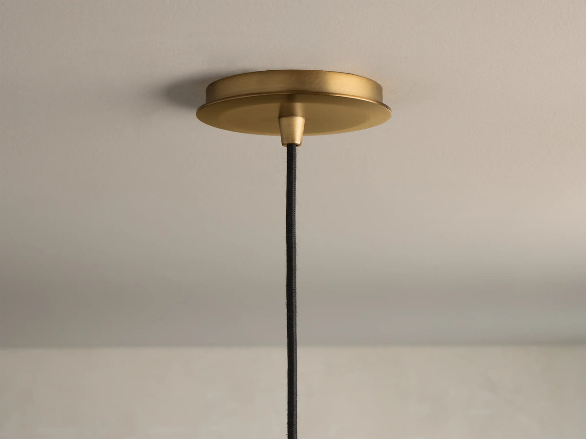 Close-up of a brushed brass pendant light ceiling canopy with a black braided fabric cord hanging down.