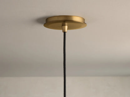 Close-up of a brushed brass pendant light ceiling canopy with a black braided fabric cord hanging down.