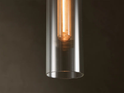 Close-up of a clear ribbed glass Pendant Light with a warm glowing Edison-style bulb inside.