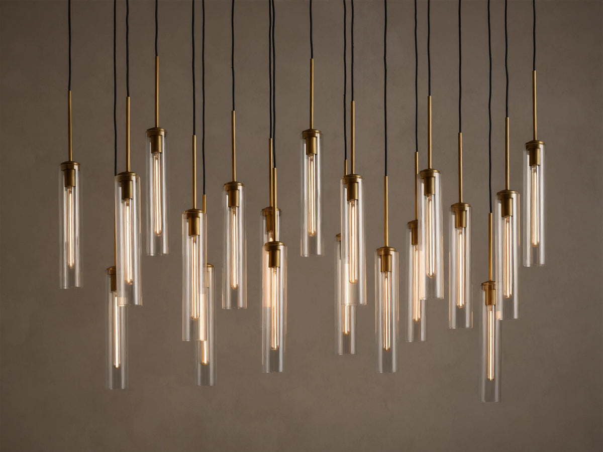 Multiple illuminated pendant lights with clear glass tubes and brass fixtures, hanging at varying heights from black cords.