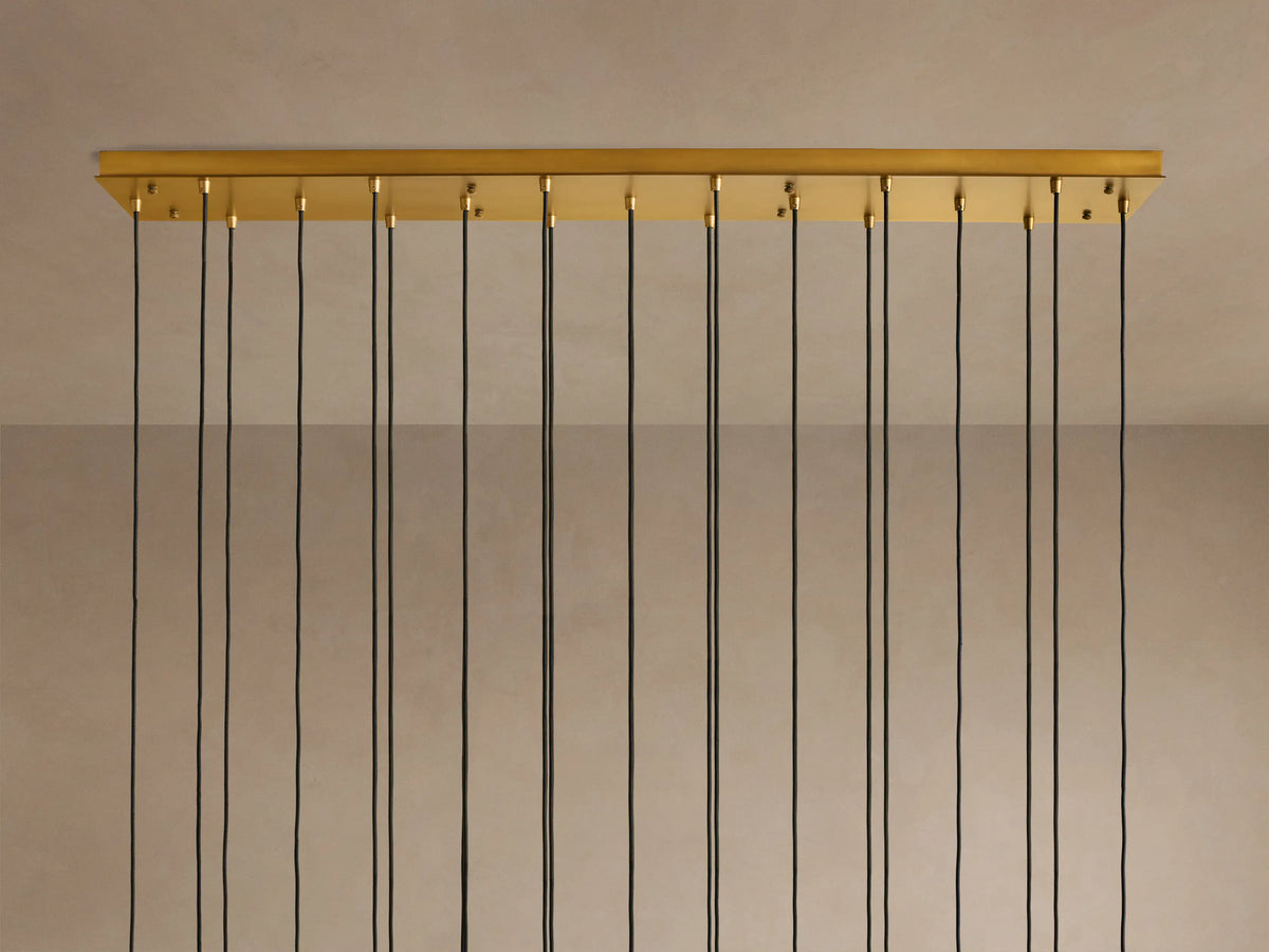 Multiple illuminated pendant lights with clear glass tubes and brass fixtures, hanging at varying heights from black cords.