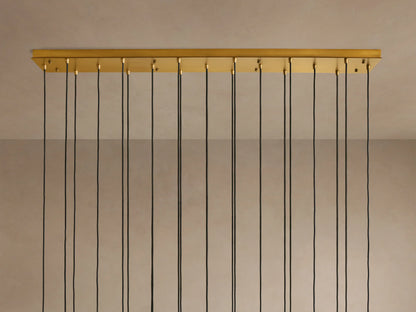 Multiple illuminated pendant lights with clear glass tubes and brass fixtures, hanging at varying heights from black cords.