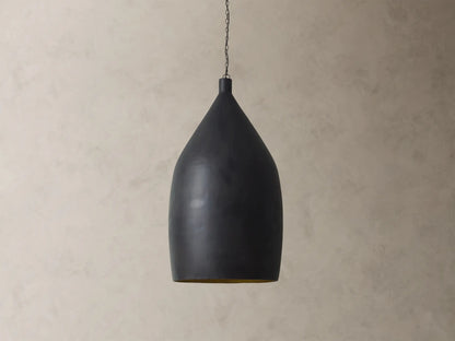 Fria Cone Pendant, a matte black conical pendant light with a golden interior glow, suspended by a chain against a textured wall.