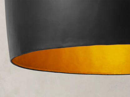 Fria Cone Pendant, a matte black inverted cone-shaped iron pendant light with a brass interior, hanging from a chain.
