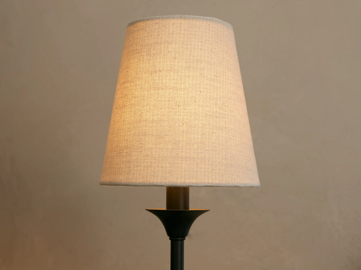 Illuminated Saige Sconce with an off-white fabric conical shade on a dark bronze or black metal base.