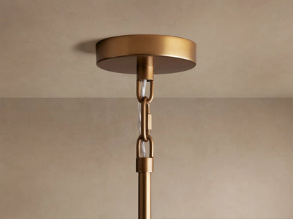 Saige Round Chandelier's brass ceiling mount with hanging chain & clear tubing for wires, against a beige ceiling.
