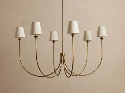 Saige Round Chandelier, brass-finished metal, with 6 elegantly curved arms, each topped with an off-white fabric shade.