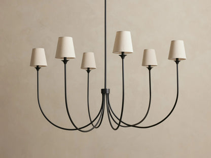 Saige Round Chandelier with 6 curved dark bronze arms & off-white tapered fabric shades, hanging against a light wall.