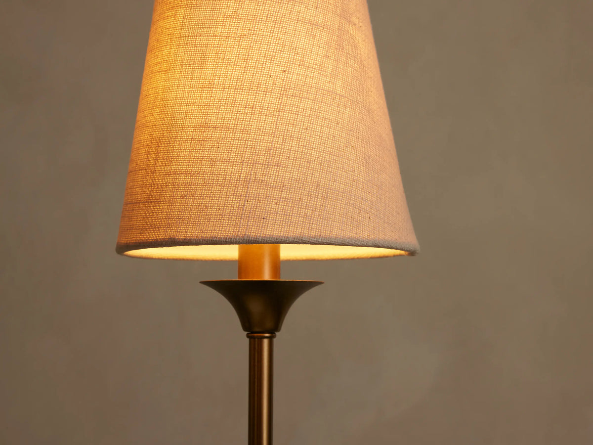 Close-up of Saige Round Chandelier. Warm light emanates from a textured off-white conical shade above a brass-toned stem.