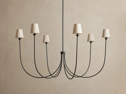 Saige Round Chandelier with 6 dark bronze curved arms, each topped with an off-white fabric shade, against a beige wall.