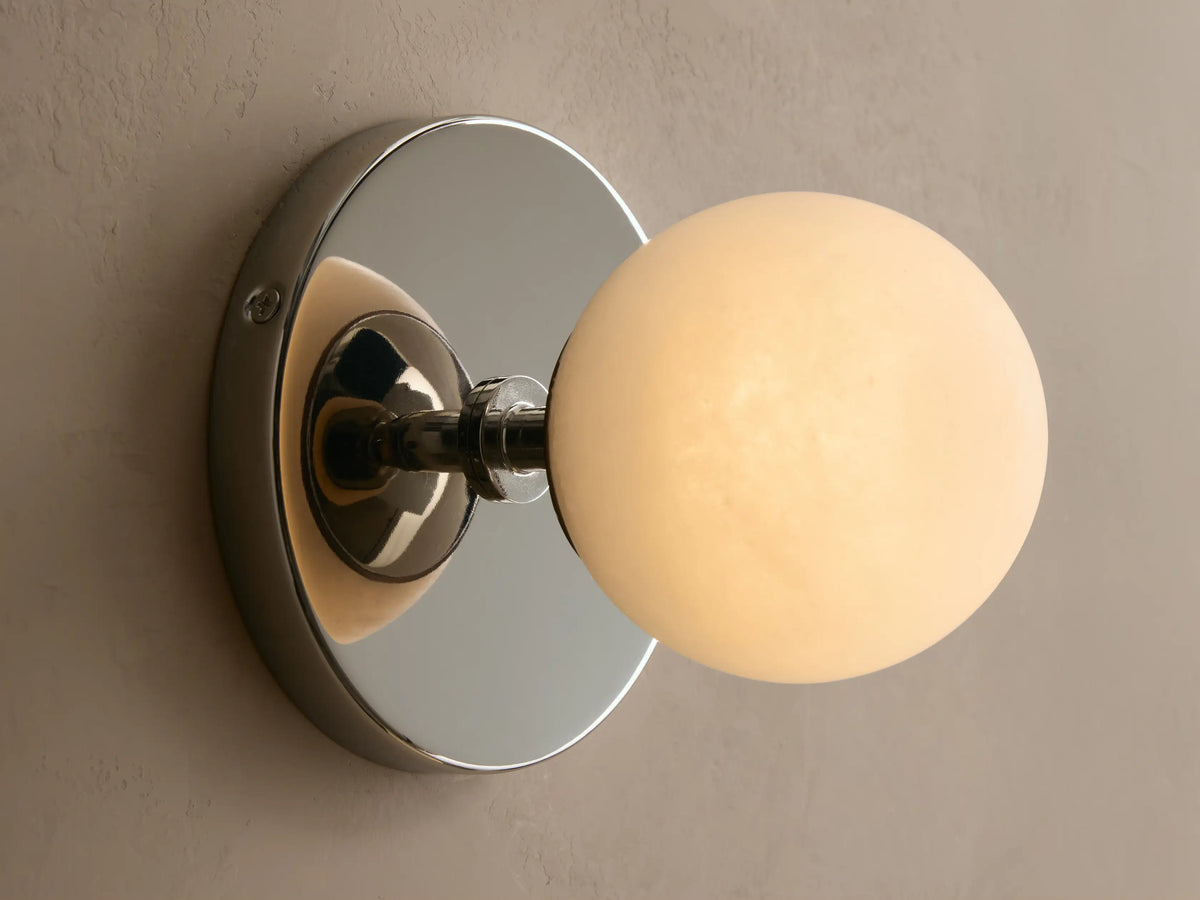 Wall-mounted light fixture with a round white glass globe and a metallic backplate. Mounted on a beige textured wall.