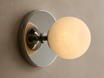 Wall-mounted light fixture with a round white glass globe and a metallic backplate. Mounted on a beige textured wall.