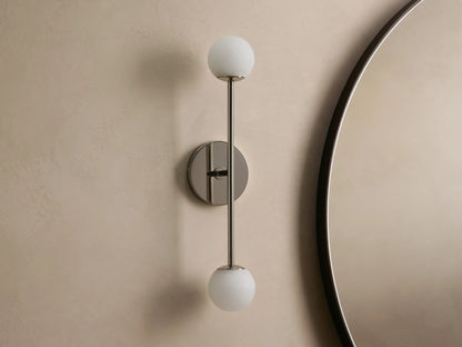 Wall-mounted lamp with a sleek metal fixture, featuring two spherical frosted glass bulbs, vertically aligned against a neutral wall.